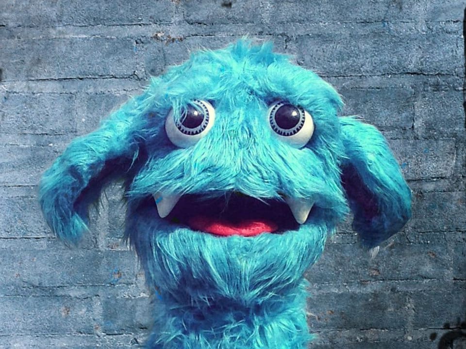 Eine blaue, zottelige Puppe mit grossen Augen.