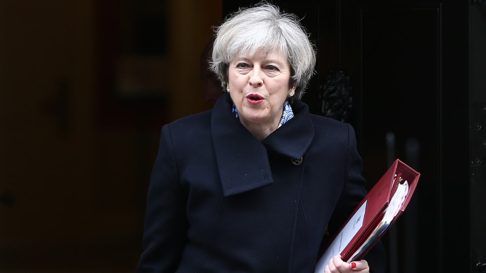 Theresa May mit einem Ordner in der Hand vor schwarzem Hintergrund.