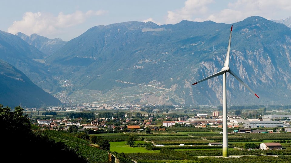 Windrad, im Hintergrund eine Ortschaft und Berge.