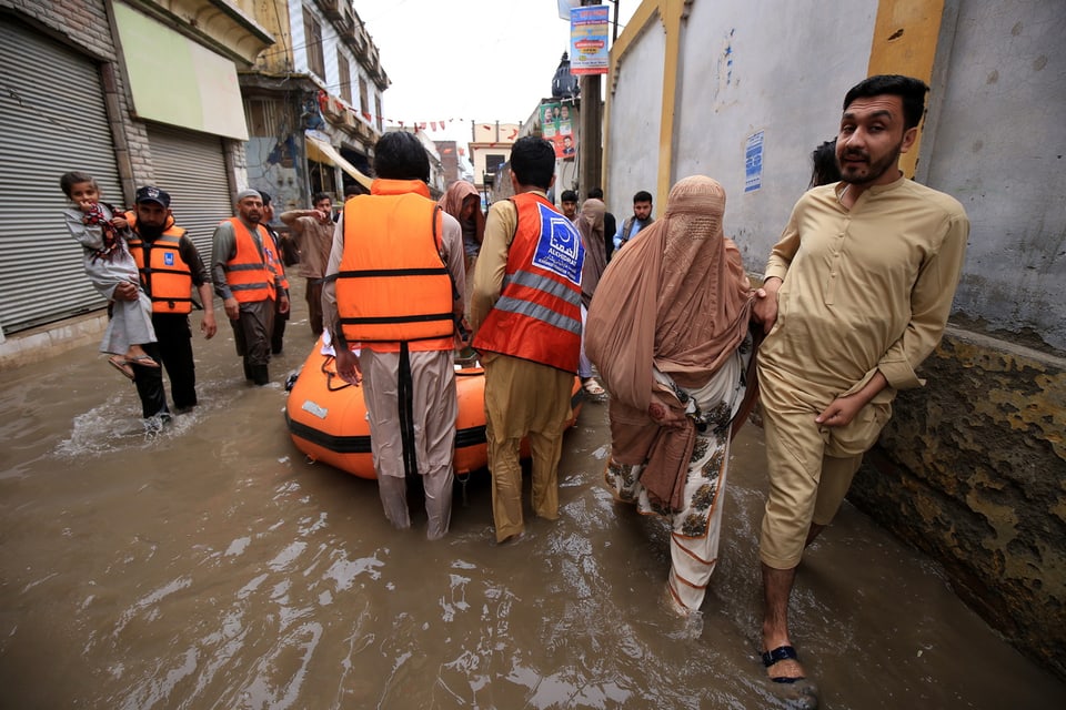 Männer in orangen Westen evakuieren Anwohnende auf der überschwemmten Strasse.