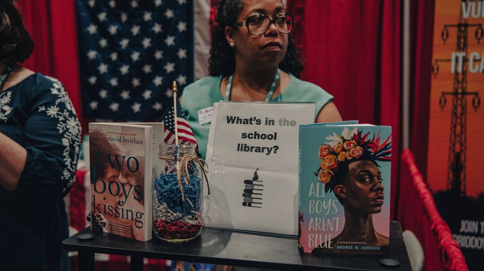 Frau mit Brille hinter mehreren aufgestellten Büchern, darunter rechts ein Cover mit der Schrift «All Boys aren't blue»