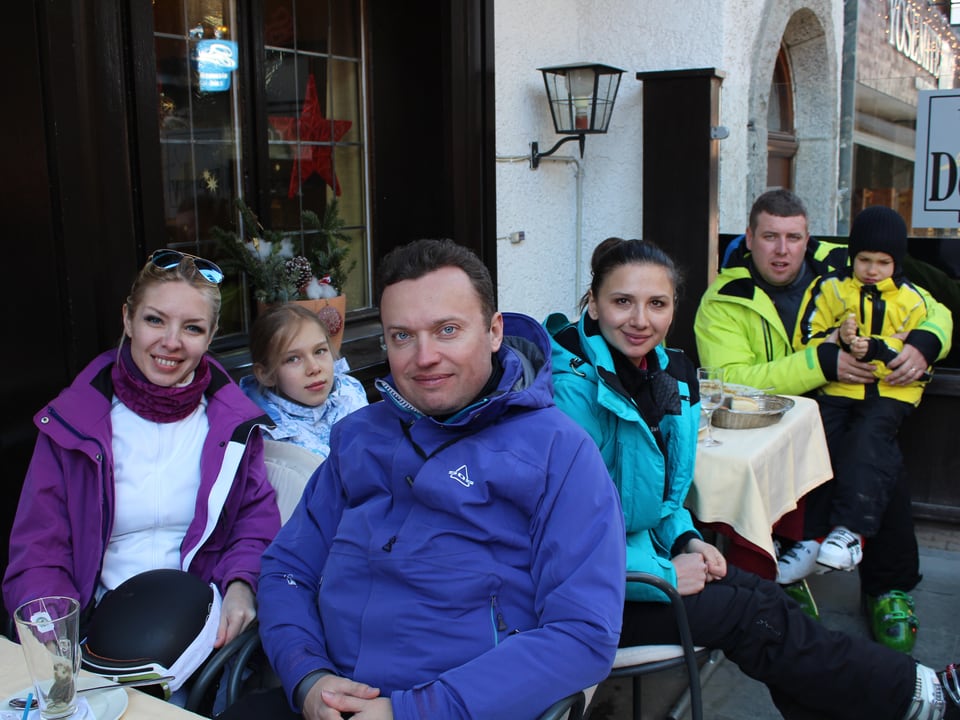 Familie sitzt in Zermatt draussen an einem Restaurant-Tisch. Sie tragen alle Skikleider.