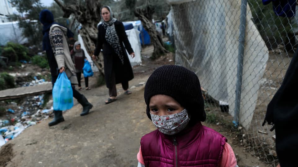 Menschen in Moria, im Vordergrund ein Kind mit Gesichtsmaske.