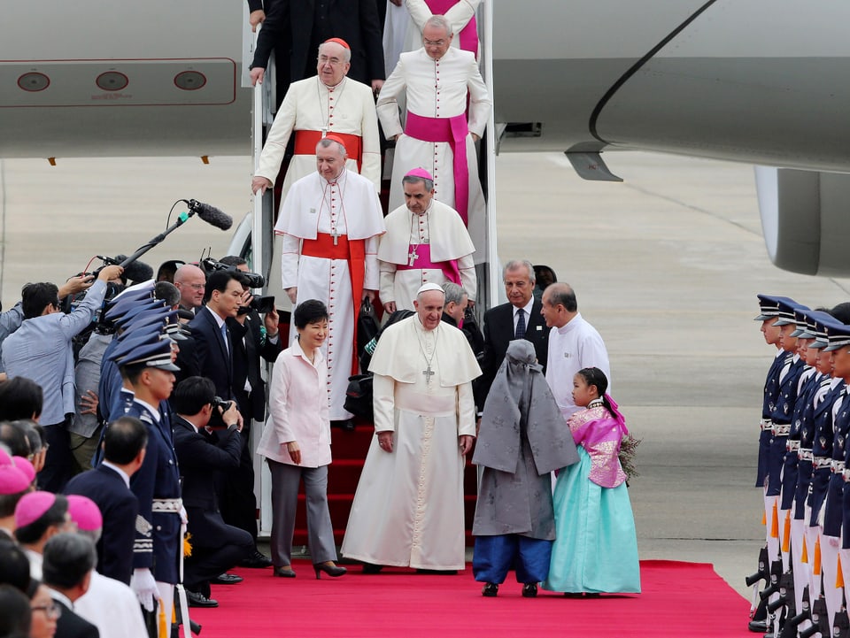 Papst tritt aus dem Flugzeug auf einen roten Teppich.