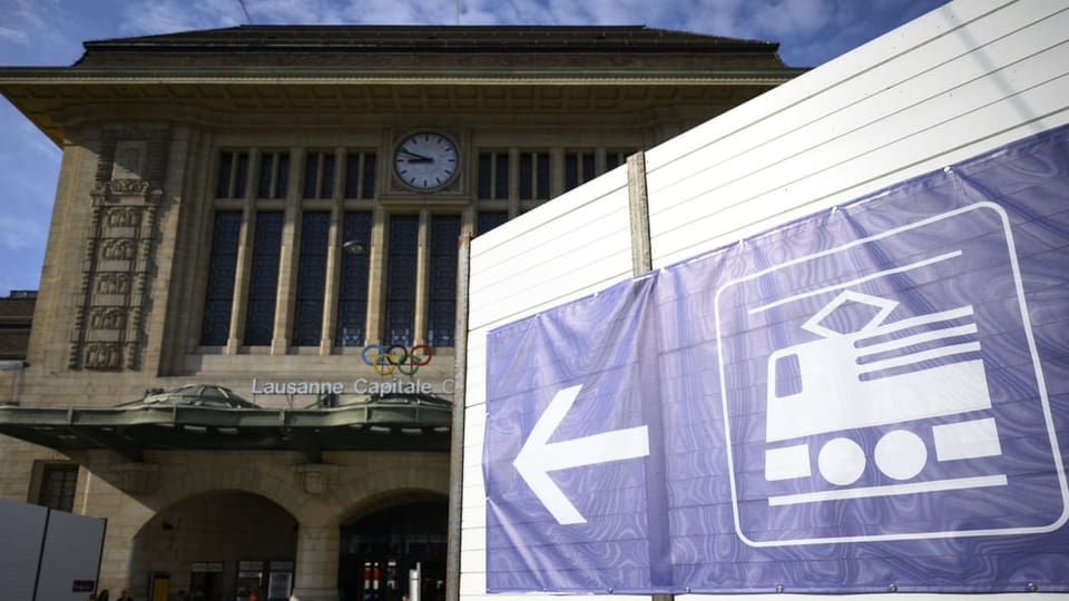 Totale auf den Bahnhof Lausanne mit einem Bauzaun. Ein Hinweisschild zeigt den Eingang in den Bahnhof an.