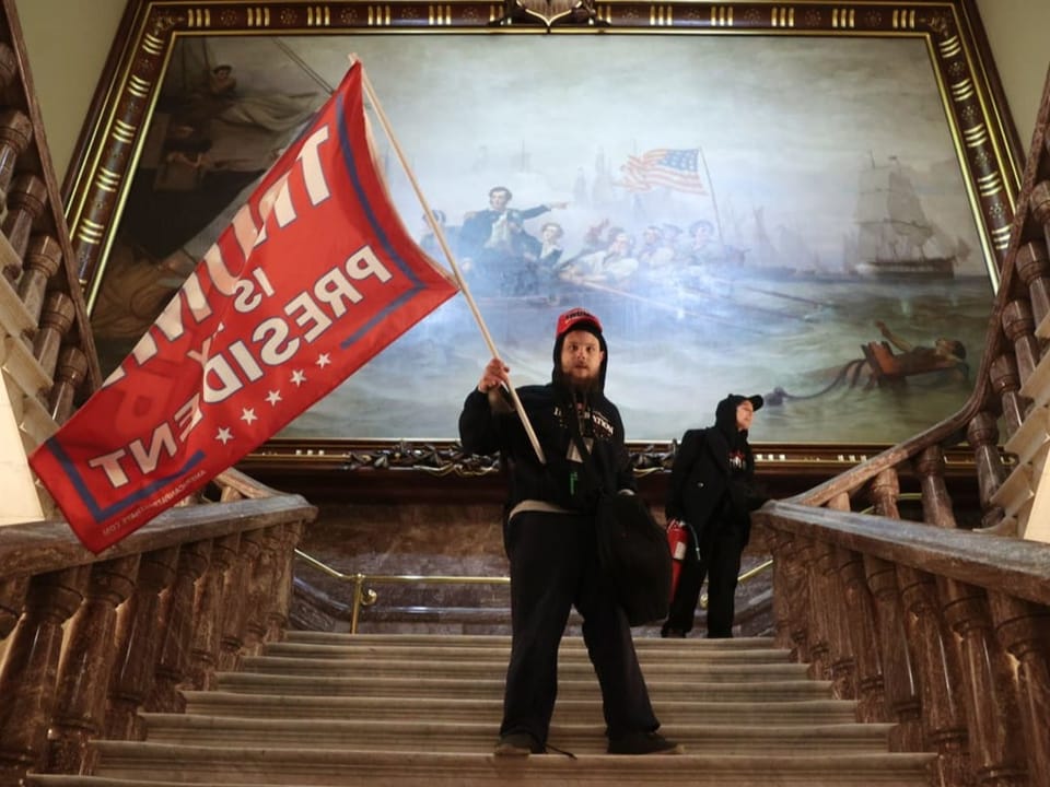 Ein schwarz gekleideter Protestierender steht auf einer Treppe und schwenkt eine rote Flagge