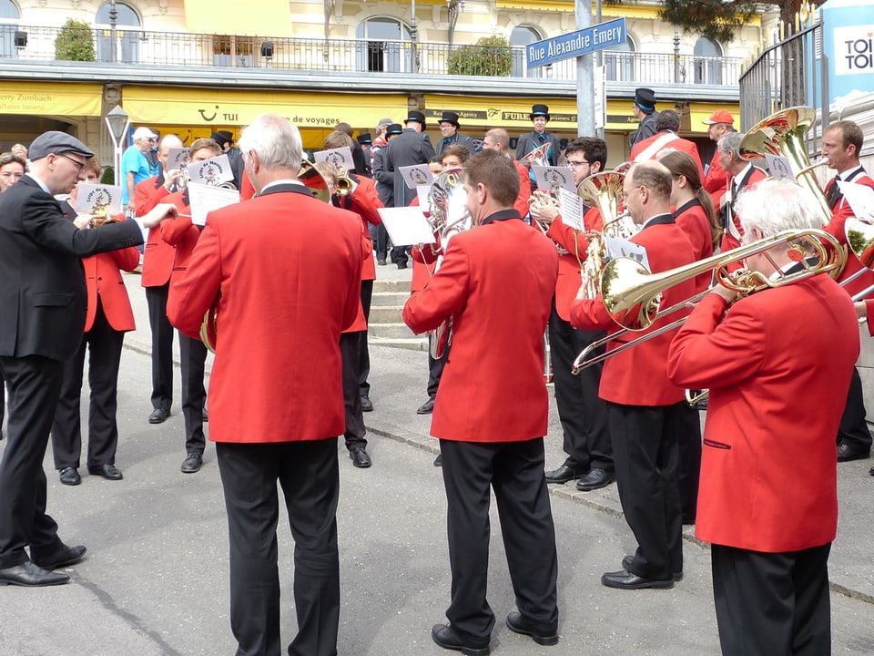 Blasmusikanten in rot-schwarzen Uniformen spielen auf einer offenen Strasse.