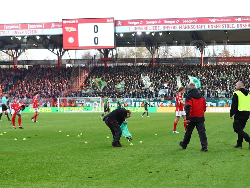 Ordnungspersonal sammelt auf das Feld geworfene Tennisbälle auf bei Union Berlin vs. Wolfsburg.