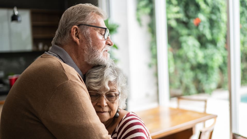 Ein Seniorenpaar in einem Esszimmer umarmt sich innig