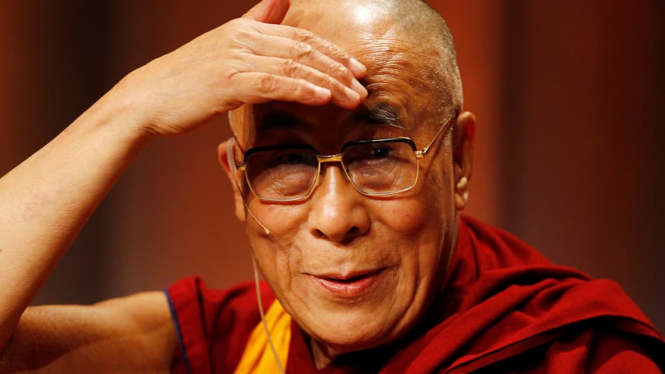 Der Dalai Lama hält sich die Hand über die Stirn, weil er geblendet wird
