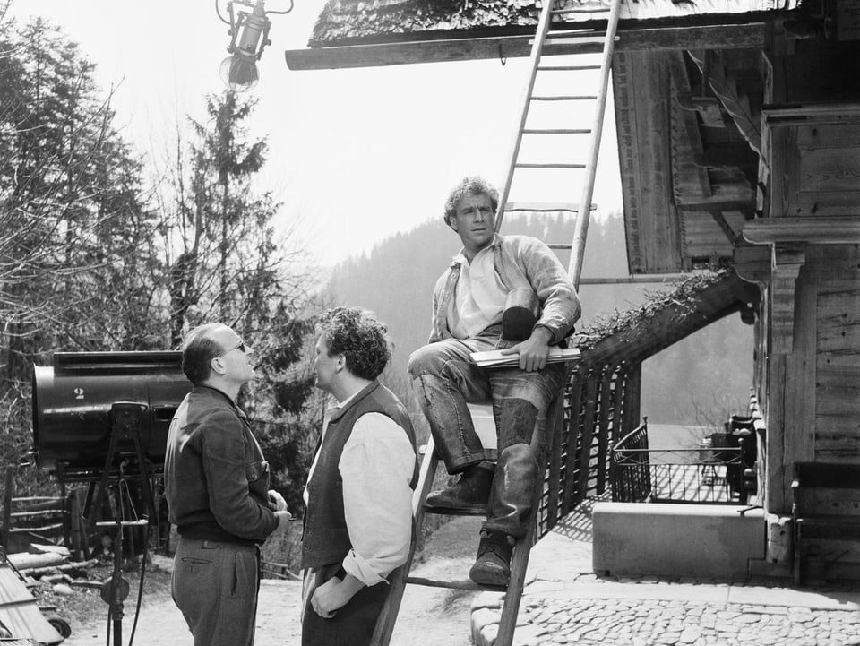 Schnyder und zwei Schauspieler befinden sich auf einem Hof in den Bergen.