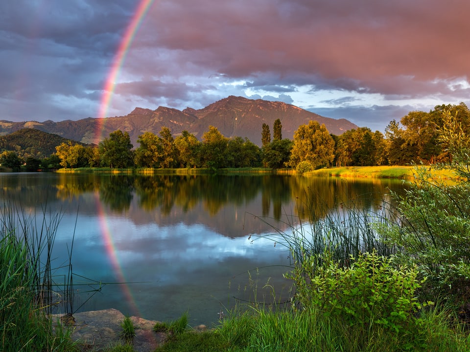 Regenbogen spiegelt sich im See.