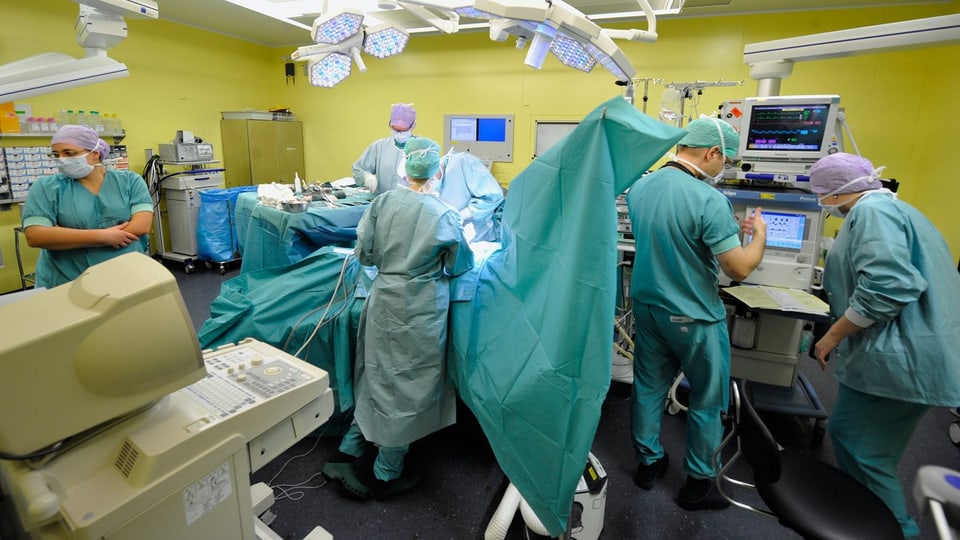 Ein Operationssaal mit vielen Ärzten. Sie tragen Mundschutz und grüne Übermänner.