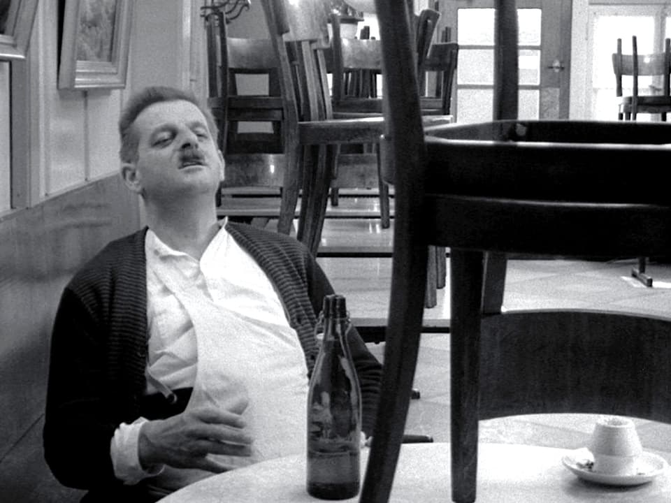Ein Mann sitzt am Tisch, vor ihm steht eine Flasche Bier.