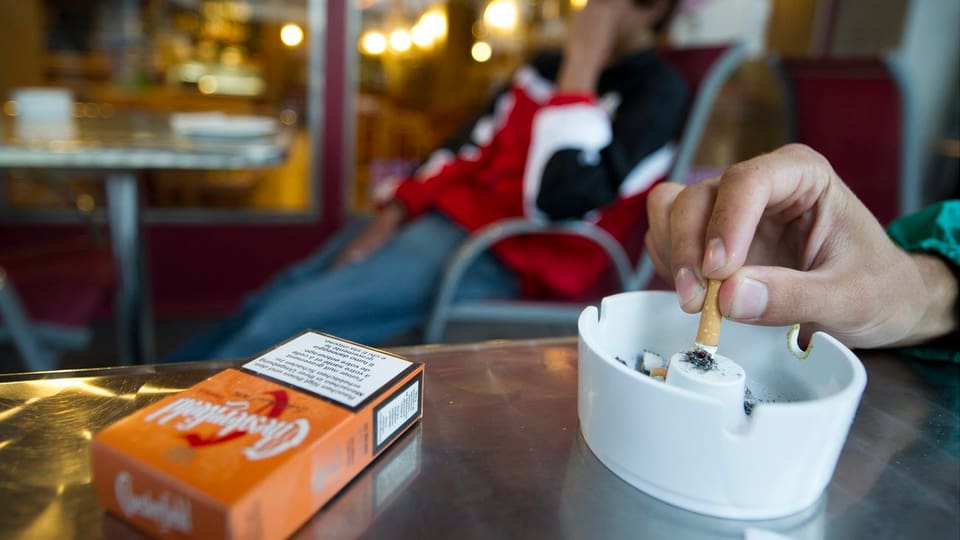 Hand drückt Zigarette in einem Aschenbecher aus.