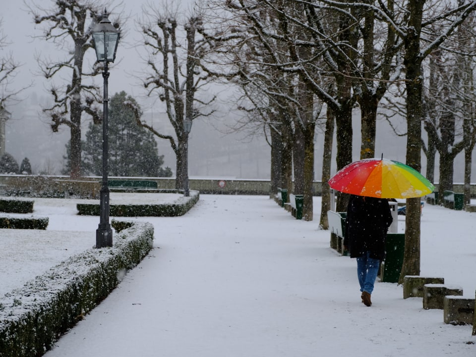 Leicht verschneite Münsterplattform in Bern mit einer Person, welche einen regenbogenfarbigen Schirm aufgespannt hat.