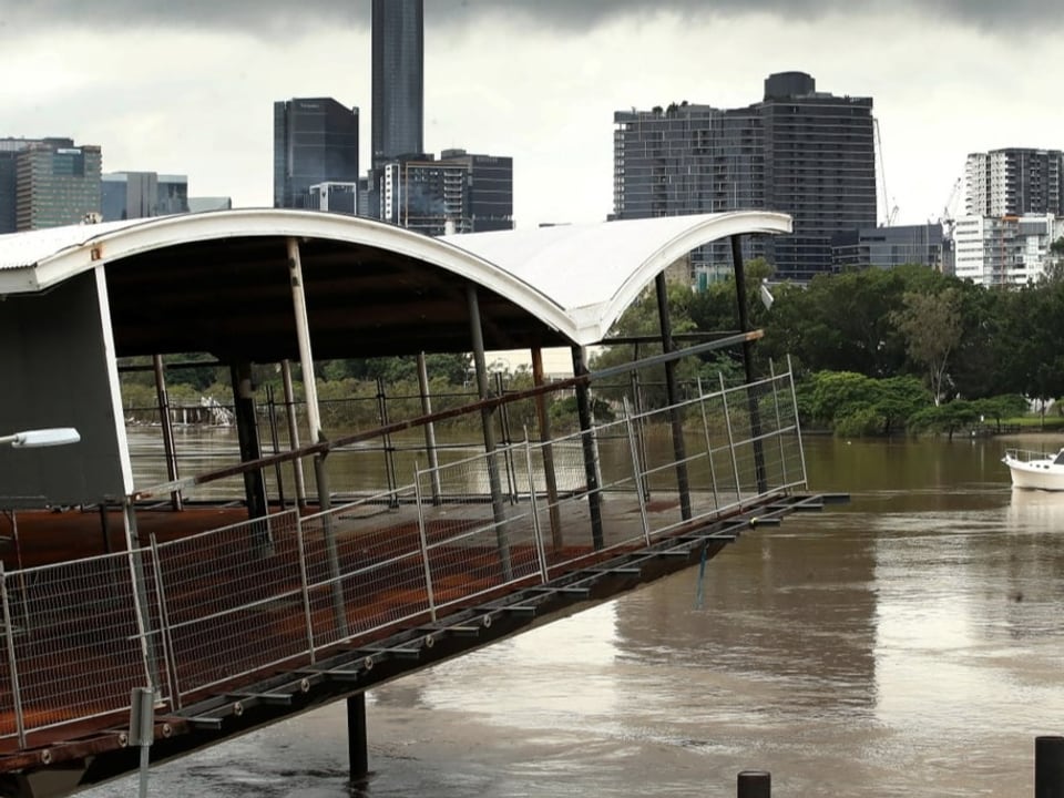 Fluss vor Stadt mit durch Flut mitgerissenem Gebäude