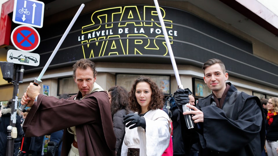 Drei Kinogänger in Star-Wars-Kostümen Laserschwertern vor einem Pariser Kino