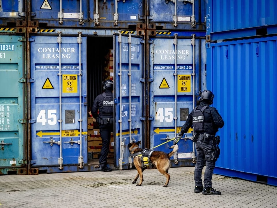 Zwei Polizisten suchen in einem Schiffscontainer mit einem Spürhund nach Drogen.