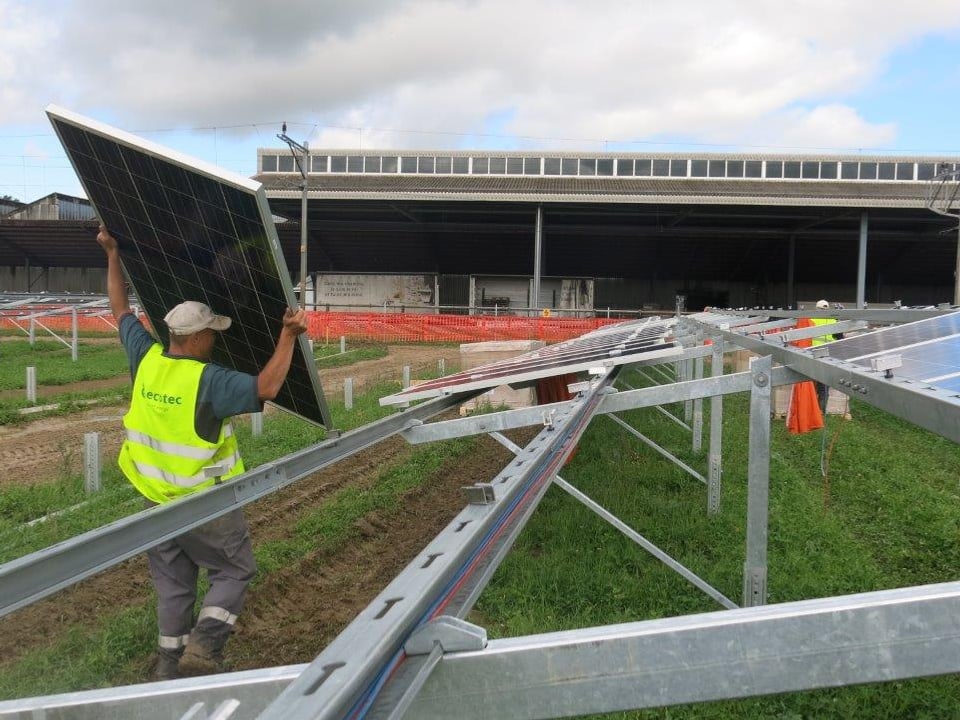 Ein Arbeiter hebt ein Solarpanel in eine Metallverstrebung. 