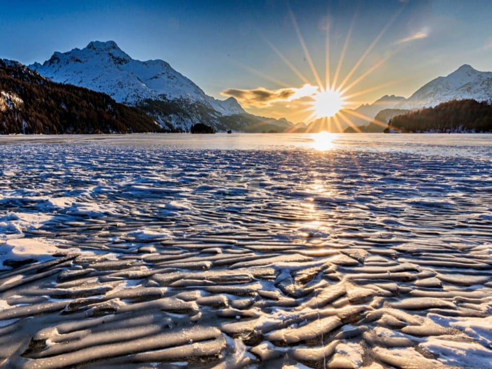 Blick über einen See mit Eisschollen auf den Sonnenuntergang im Bergtal. 