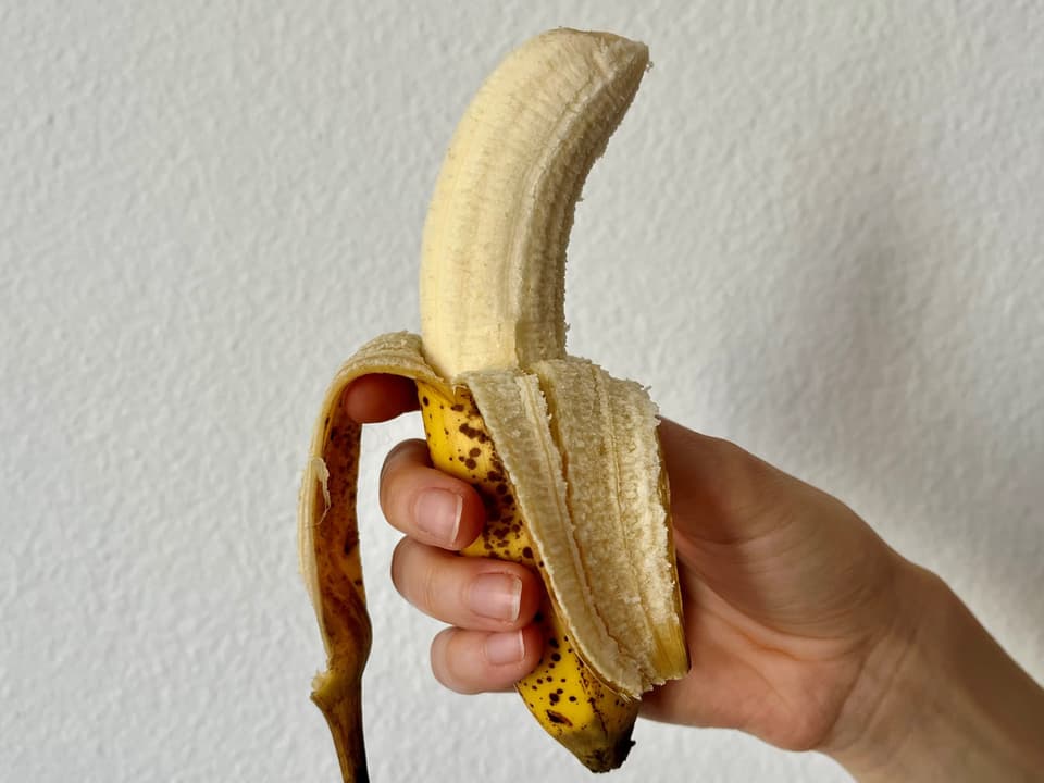 Hand hält eine halb geschälte Banane.