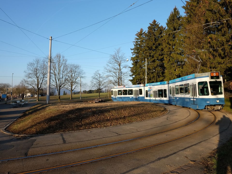 Ein blau-weisses Tram steht bei strahlendem Sonnenschein an der Haltestelle.