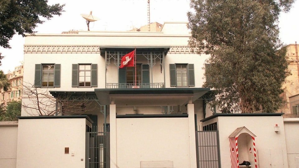 Front der Schweizer Botschaft in Kairo mit Schweizer Fahne und Satellitenschüssel auf dem Dach.