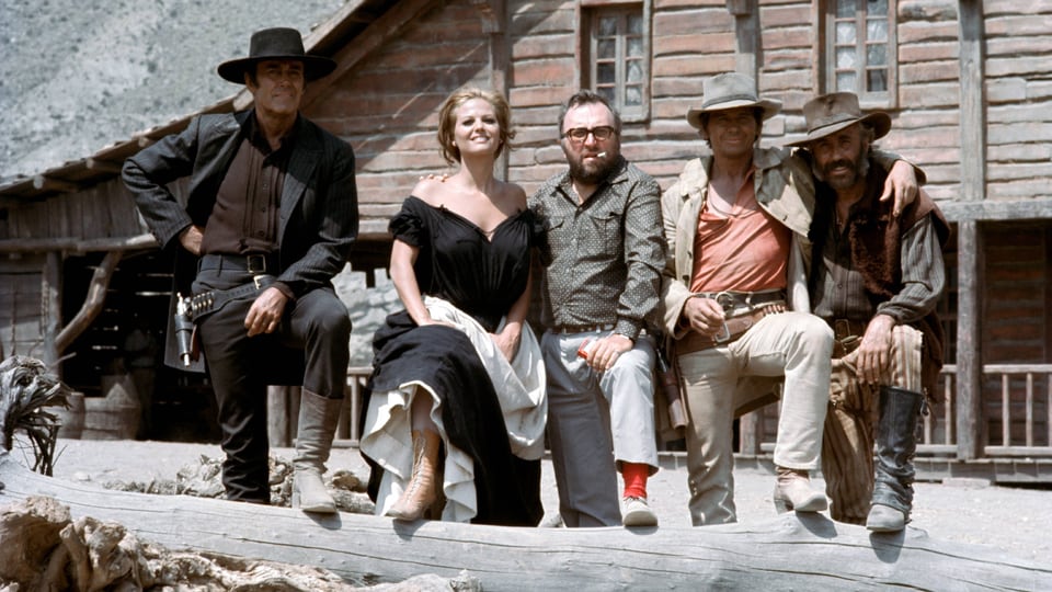 Vier Männer und eine Frau stehen in der Wüste vor einem Haus.