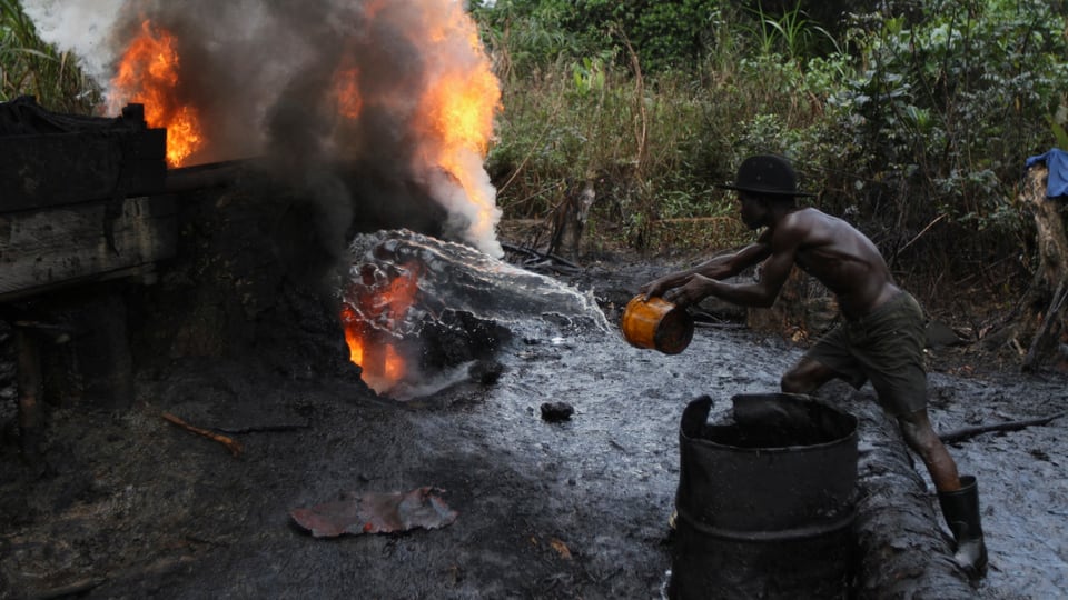 Ein Mann löscht eine Feuer einer illegalen Ölraffinerie im Nigerdelta.