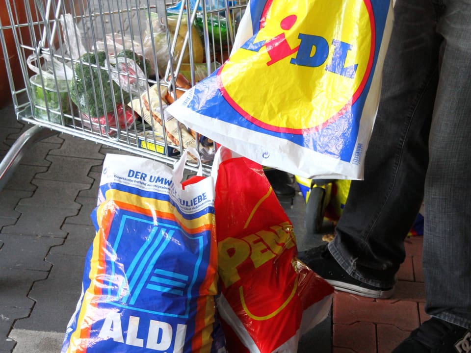 Ein Mann füllt seine Einkäufe aus einem Wagen in Plastiksäcke von Lidl und Aldi.