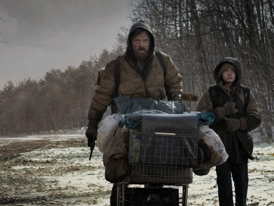 Ein Mann und ein Junge schieben einen Einkaufswagen durch eine winterlich-depressive Landschaft