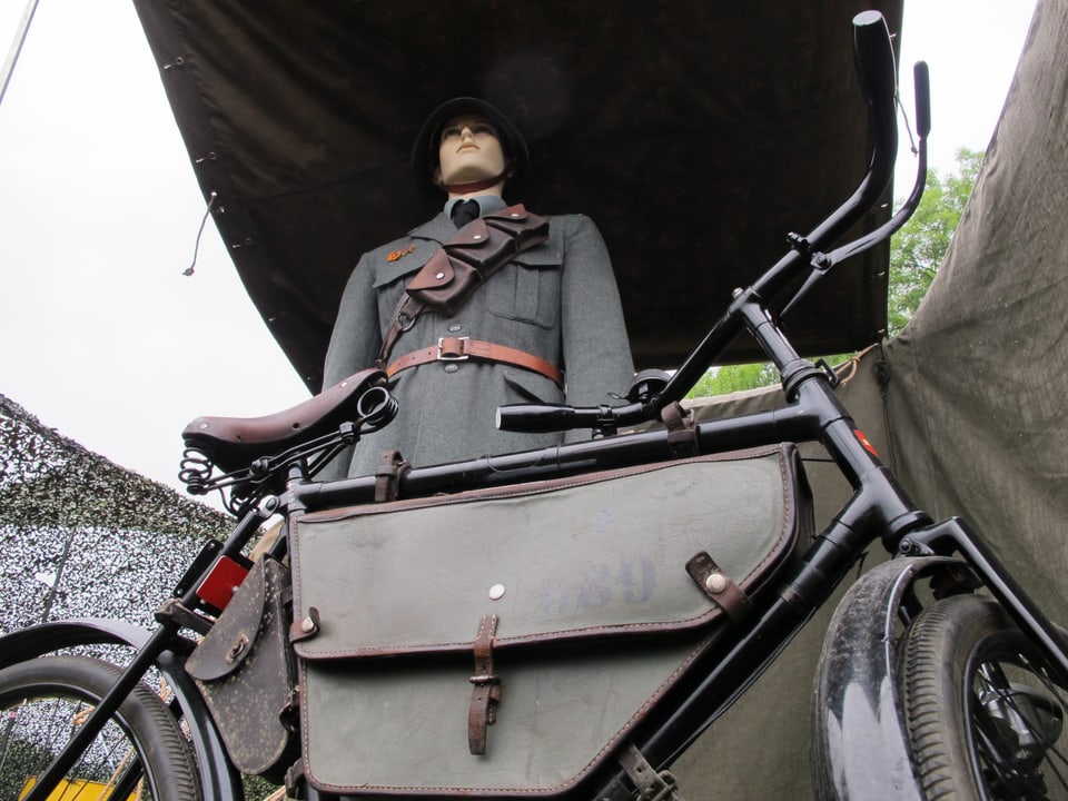 Eine Puppe in der Uniform der Fahrradfahrer, im Vordergrund steht das Armeevelo.