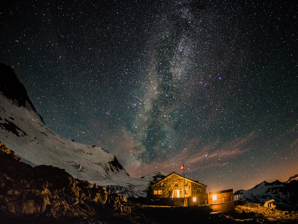 Leuchtender Sternenhimmel und leuchtende Berghütte.