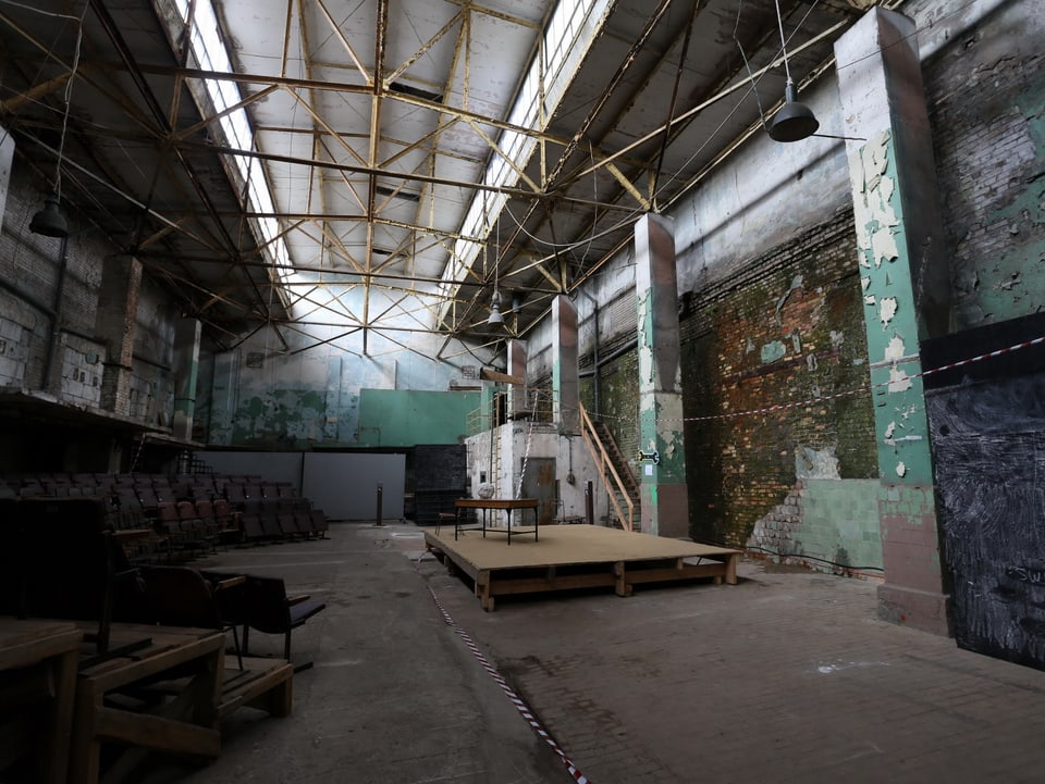 Eine kleine Bühne mit Theaterbestuhlung in einer alten, etwas heruntergekommenen Fabrikhalle.