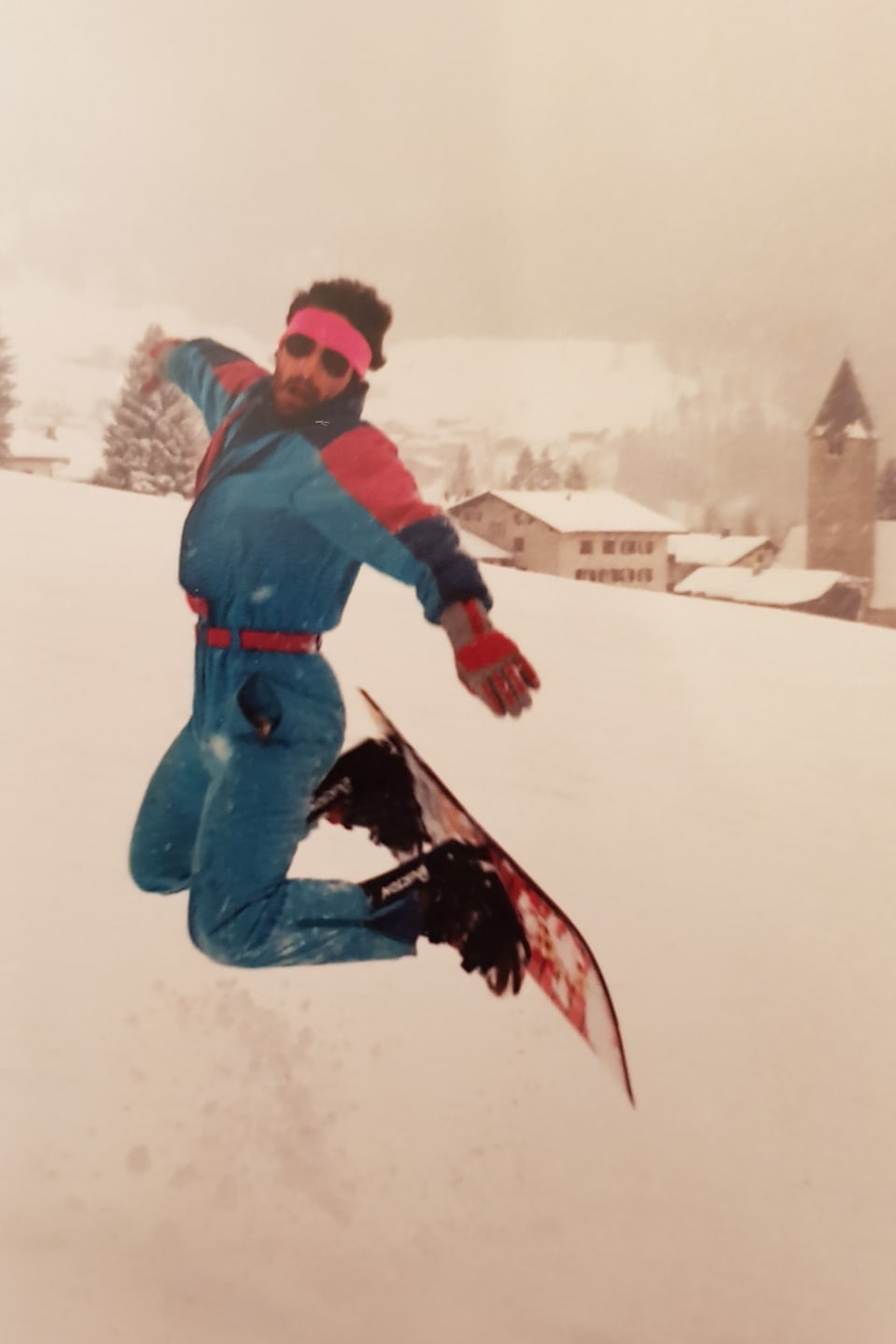 Ein Mann Hüpft im Stand in die Luft und zieht das Snowboard zurück.