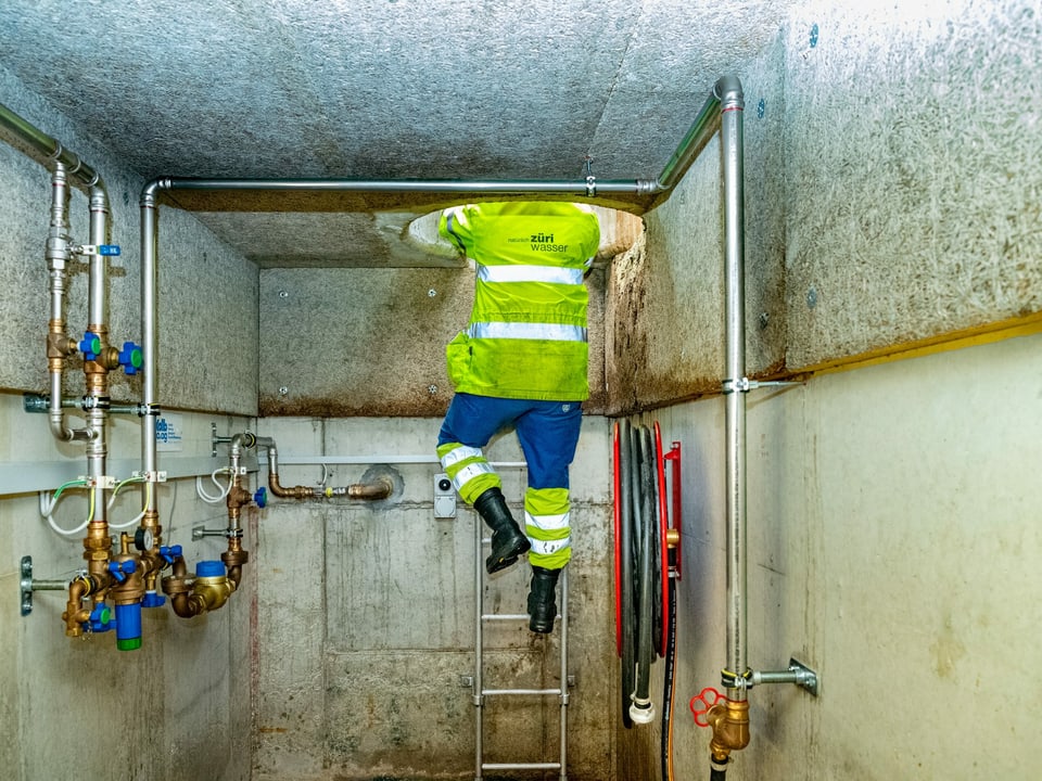 Mann steigt Leiter herunter in einen Schacht mit Wasserleitungen