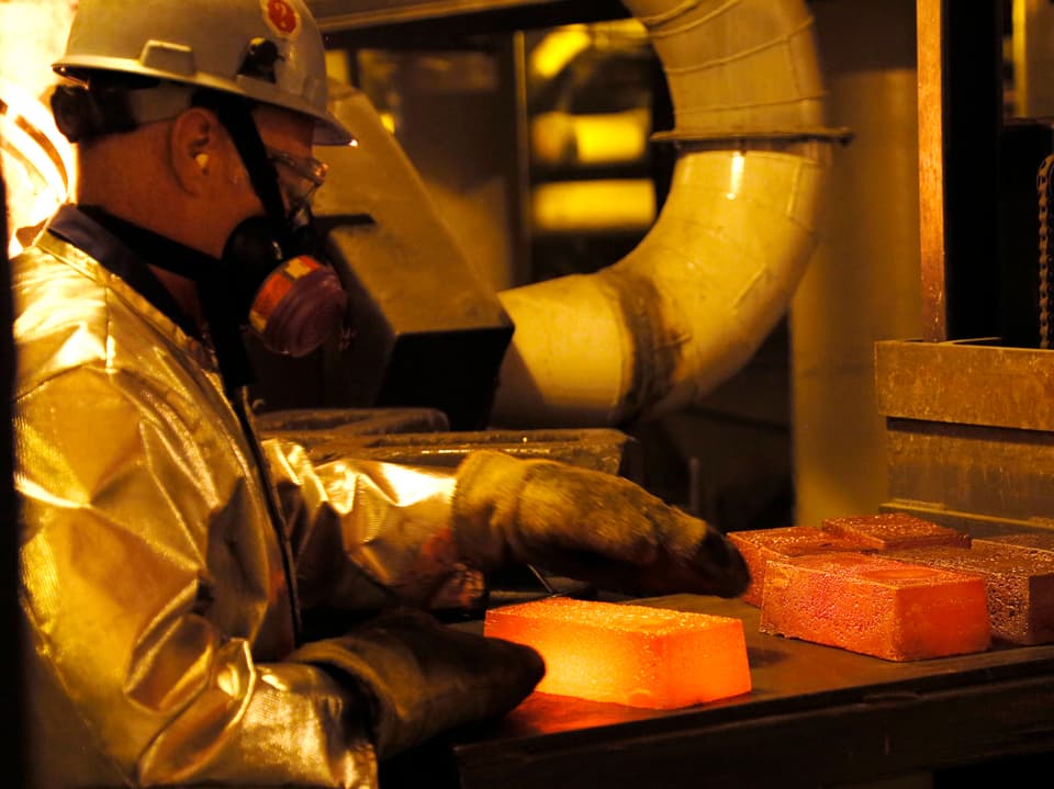 Ein Arbeiter in Wärmeschutzanzug schichtet glühende Goldbarren auf eine Ablage.