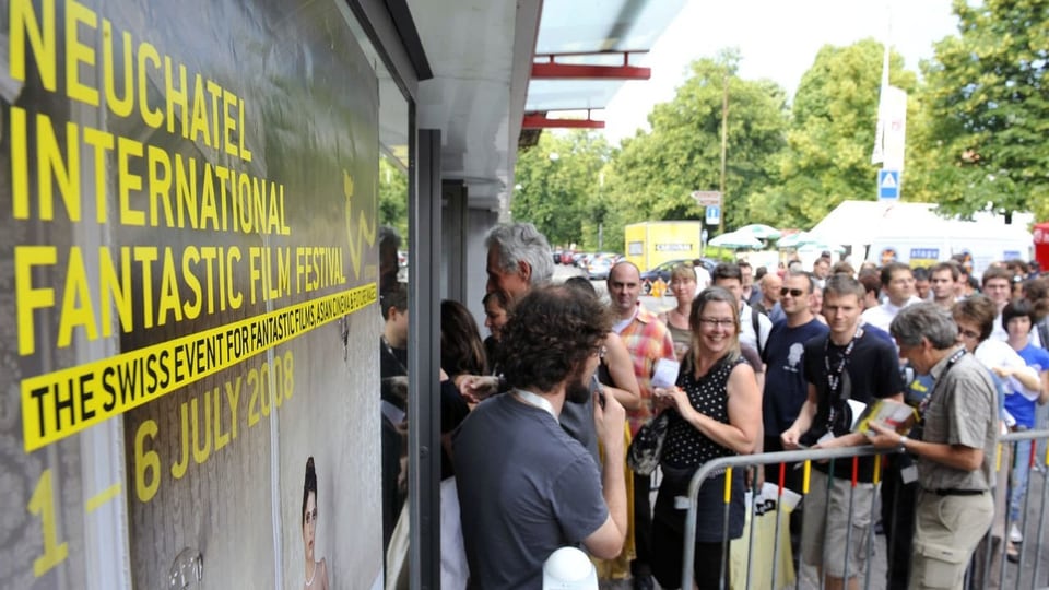 Ein grosse Anzahl Menschen steht vor einem Gebäude und wartet auf Einlass.