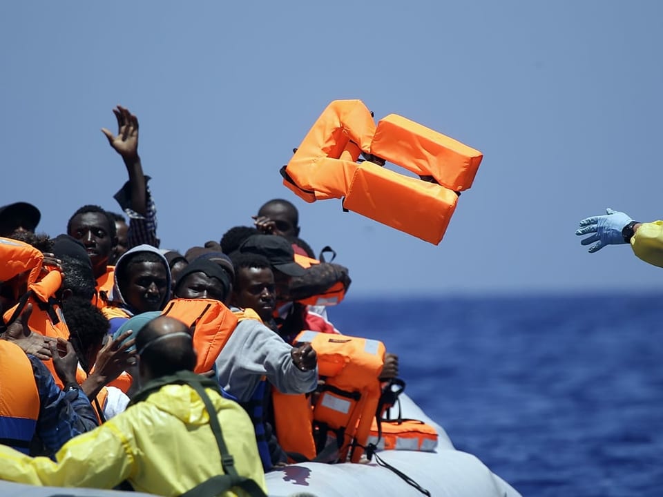 23.6.2015: Ein belgischer Soldat wirft Migranten in einem Gummiboot vom Marine-Schiff Godetia aus Schwimmwesten zu. An diesem Tag nahm alleine das belgische Schiff vor der Küste Libyens hunderte Geflüchtete auf und brachte sie an Land. 