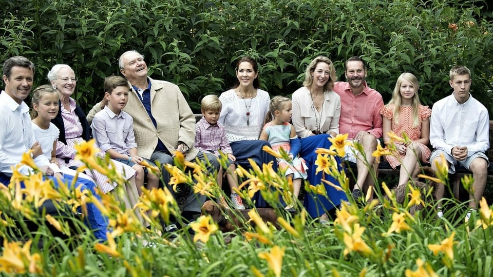 Bild der Königsfamilie. 12 Personen sitzen im Grünen auf einer Bank.