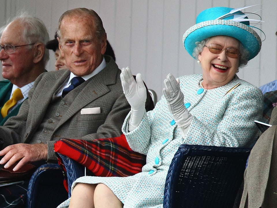 Ein älterer Mann im braunen Blazer lacht in die Kamera, neben ihm eine ältere Frau in blauem Anzug.