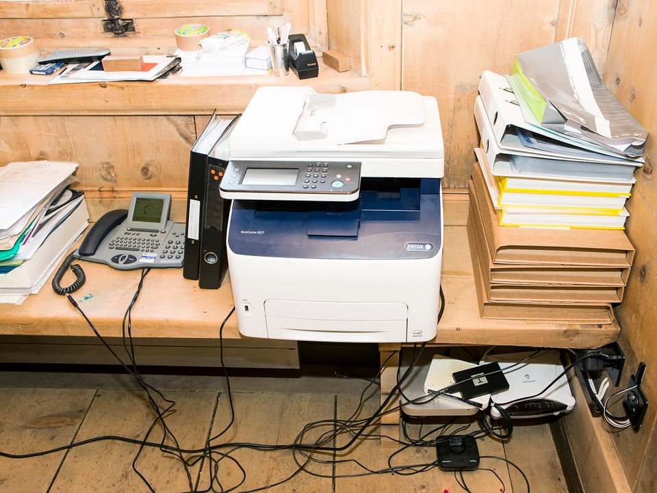 Ein Telefon, ein Drucker, Ordner und Papierunterlagen auf einer Holzbank