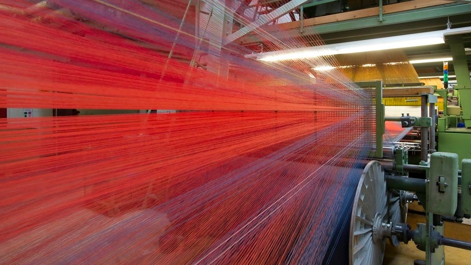 Rote Garnfäden laufen in eine Plüschwebmaschine.
