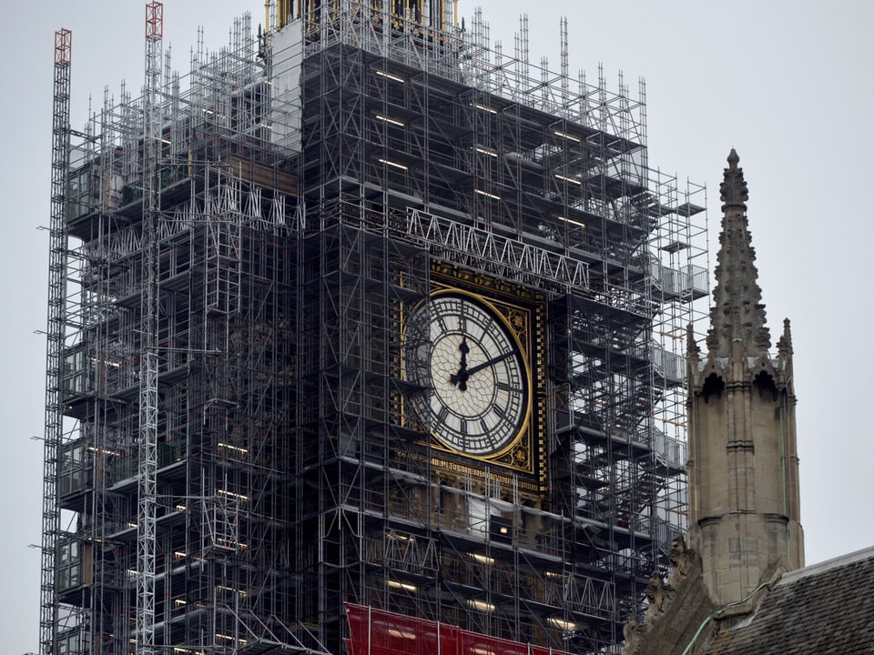Der Big Ben ist umhüllt von einem Baugerüst. Das Zifferblatt ist erkennbar.