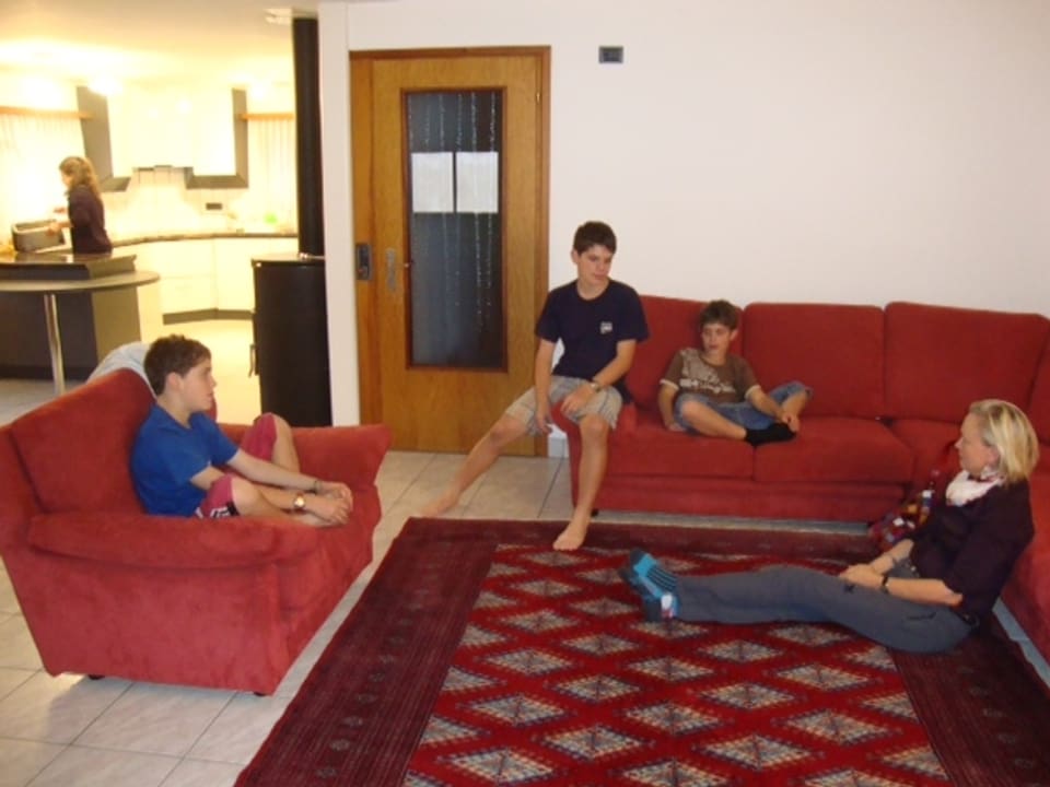 Lernsituation. Kinder sitzen im Wohnzimmer auf dem Sofa, die Sprachlehrerin am Boden auf dem Teppich.