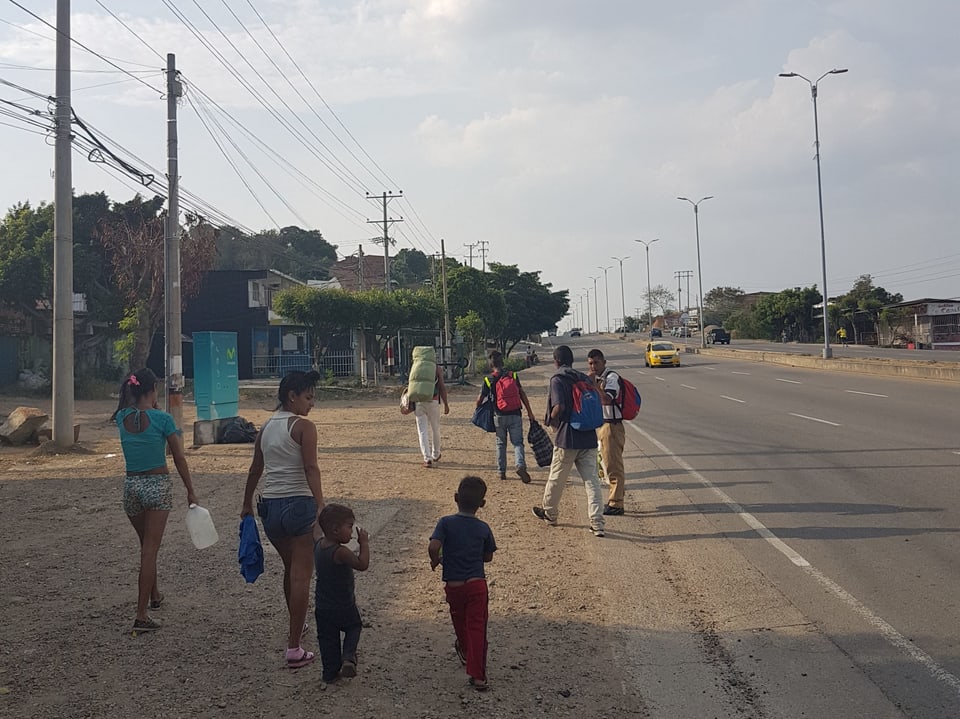 Eine Gruppe Venezolaner laufe neben einer Strasse. Es sind junge Eltern mit ihren Kindern.