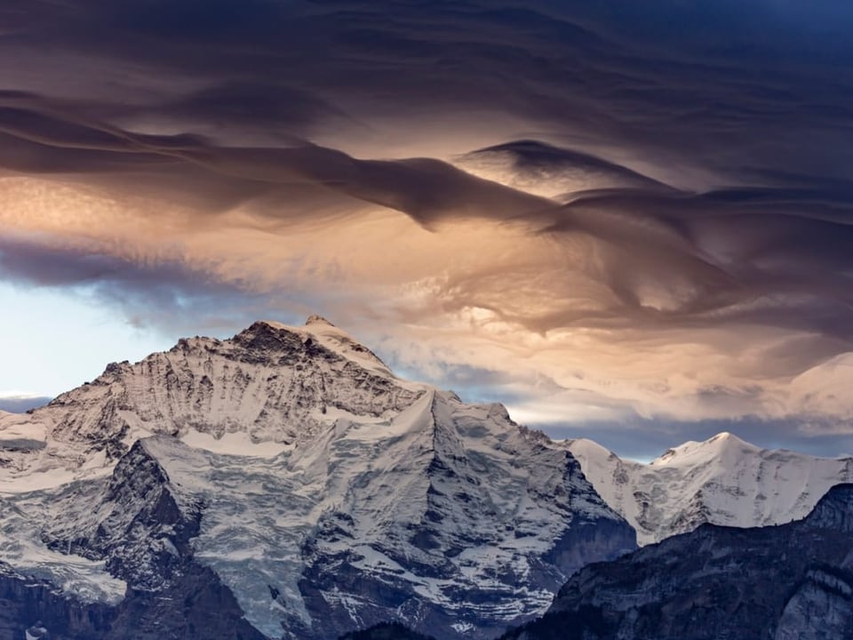 Gewellte Wolken über verschneiten Bergen