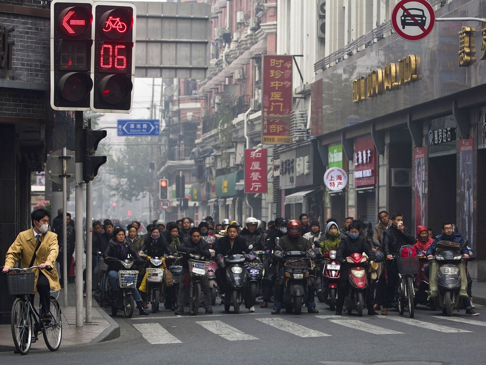 Dutzende Menschen auf Scootern warten vor einer roten Ampel.
