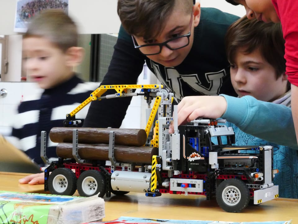 Drei Jungen spielen mit einem Lego-Truck mit Kran und ausfahrbaren Stützen.